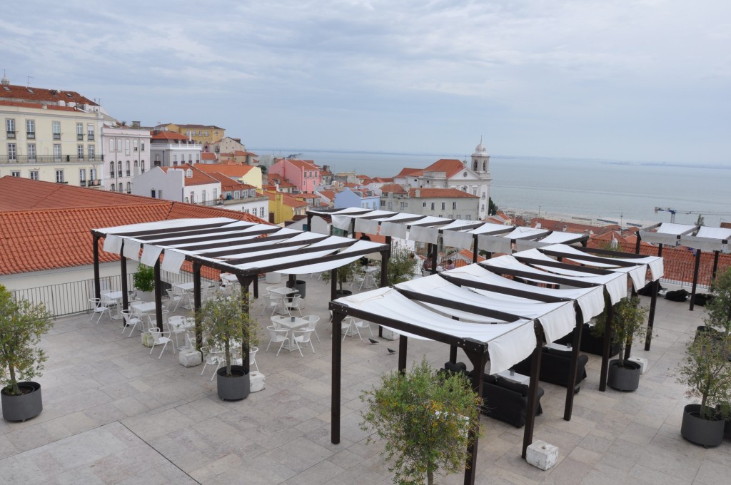 O rooftop de um hostel em Lisboa, com vista para o mar, mesas e cadeiras Visitando Lisboa com pouca grana