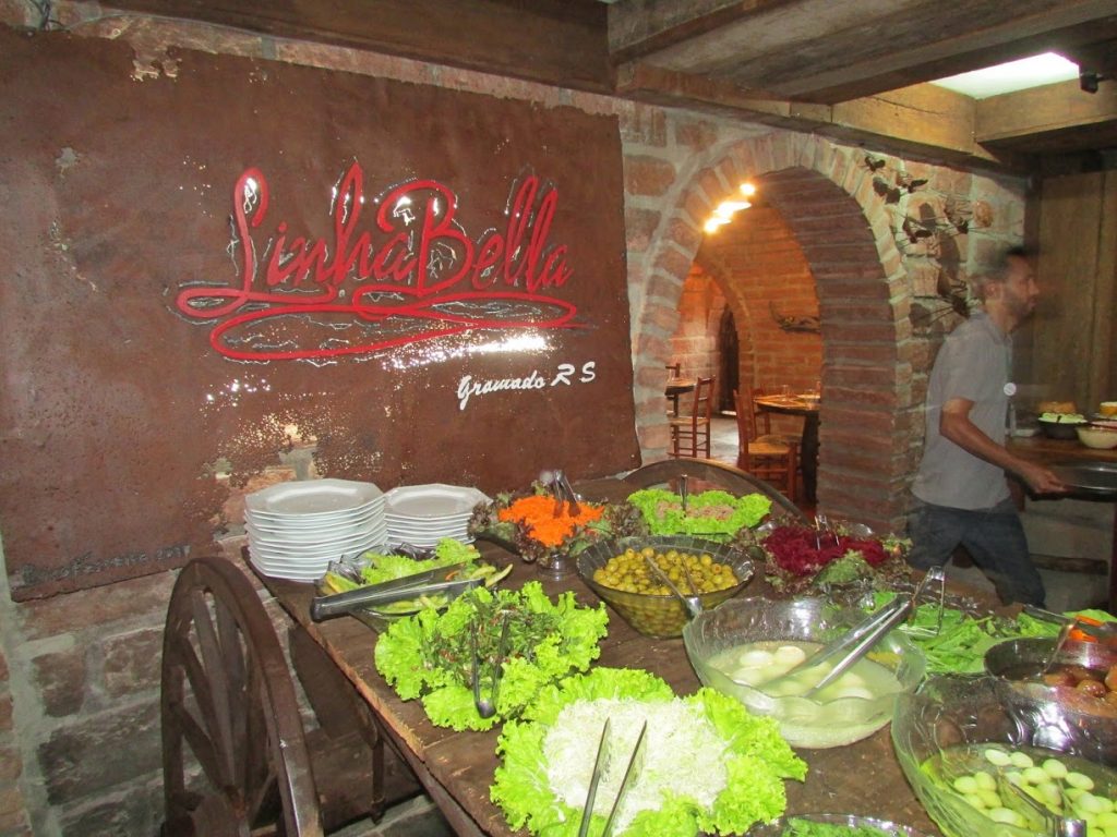 bufê de saladas com o símbolo do restaurante Linha Bella ao fundo em uma parede