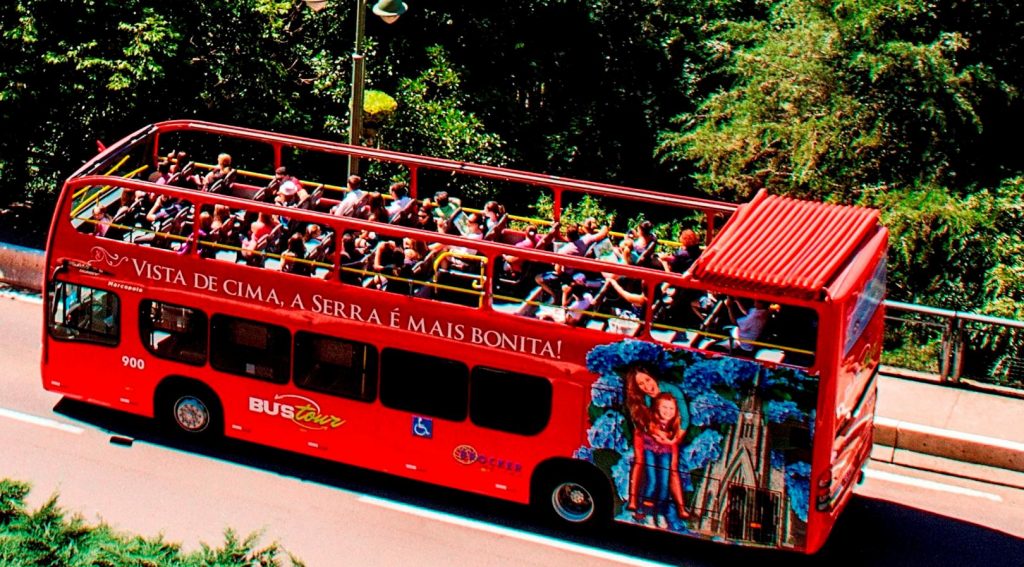 ônibus turístico vermelho com teto aberto em estrada de asfalto Bustour