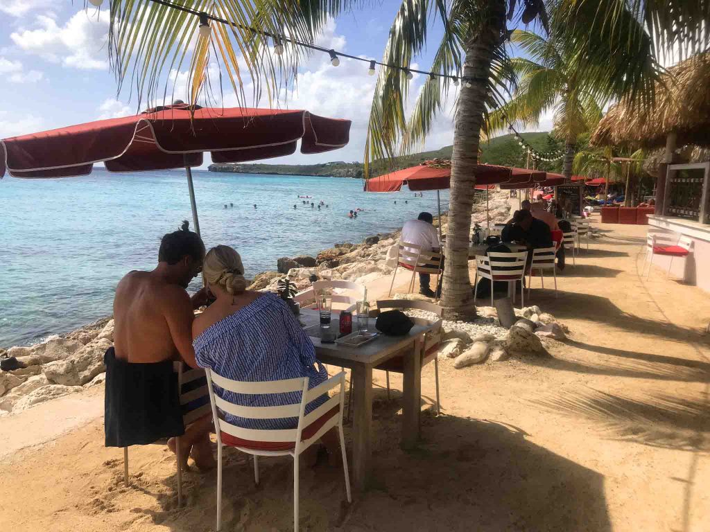 Mesas do restaurante em Curaçao de frente para o mar com cadeiras e pessoas comendo restaurantes em curaçao