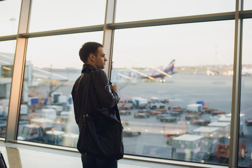 homem olhando pela janela de um aeroporto os aviões estacionados voos mais longos