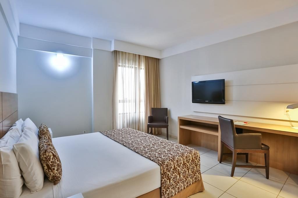 Um dos quartos do hotel em Salvador, com cama, cadeiras, televisão, e mesa