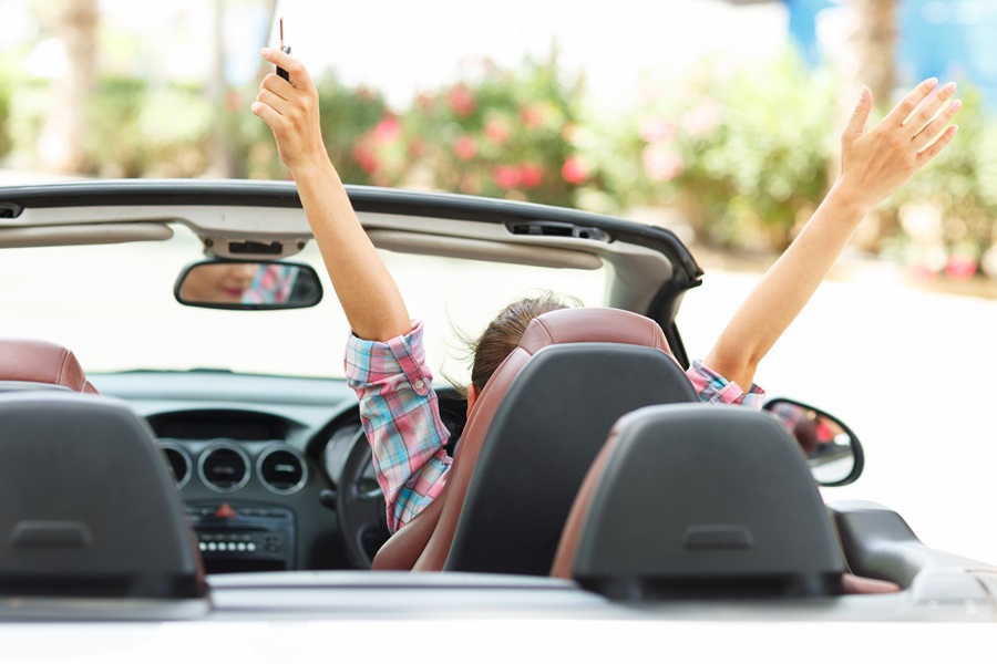 jovem com as mãos ao alto segurando uma chave, sentada no carro conversível em um dia de sol Nova York; hotéis em Nova York; Onde ficar em Nova York