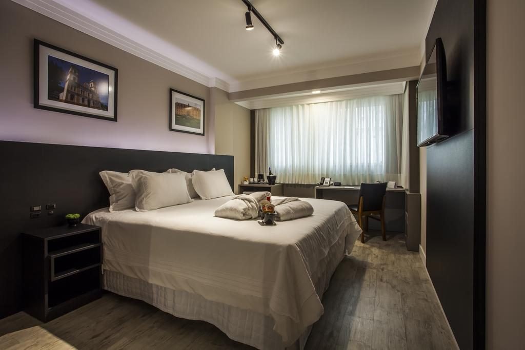 quarto de hotel com cama de casal, mesa e televisão hospedagem em Balneário Camboriú