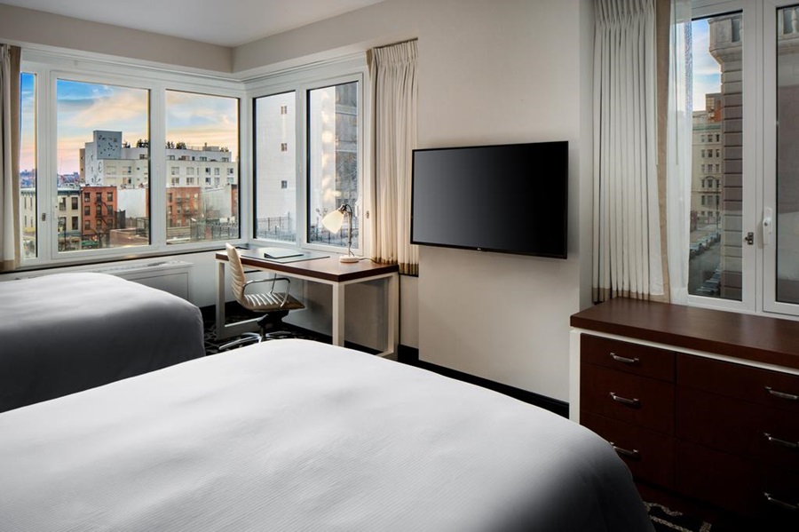 O quarto de um hotel com camas tv mesa e cadeira