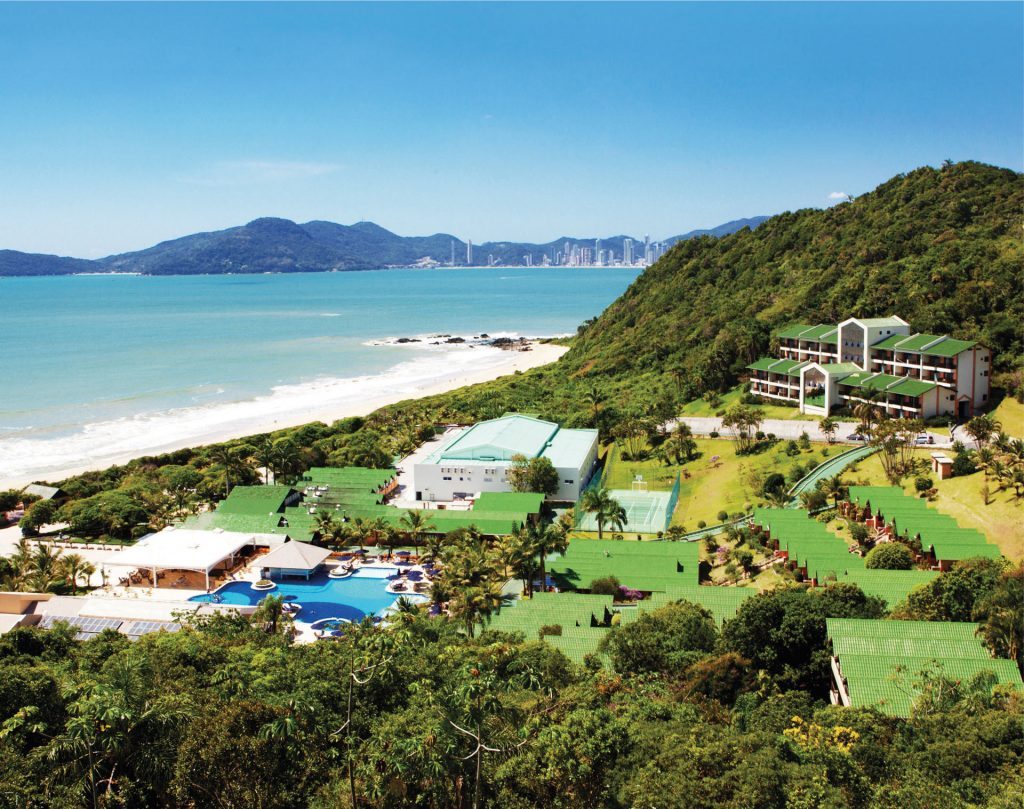 Vista aérea do Infinity Blue Resort com piscina, arvores e praia ao fundo Infinity Blue