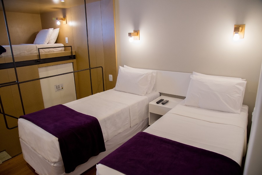quarto com três camas sendo duas brancas box com cobertor roxo na ponta e uma outra cama ao lado em formato de beliche Villa 25 Hostel