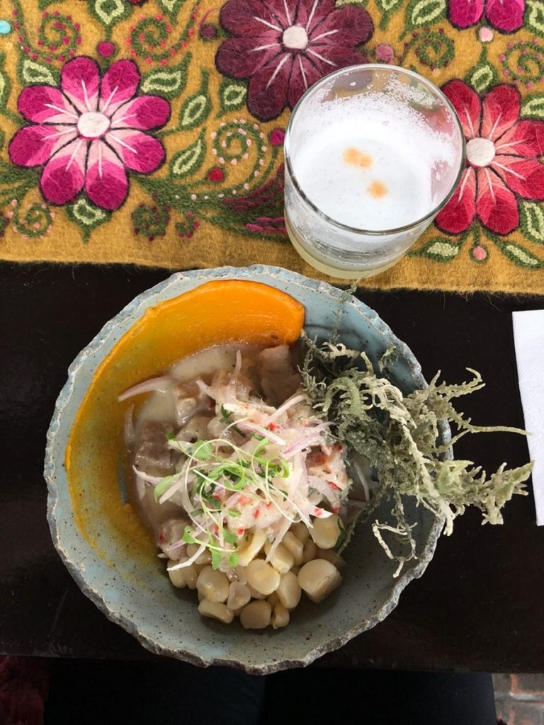 O típico prato peruano chamado ceviche com peixe cru, cebola, molho com limão, semente e uma bebida na mesa em cima de uma toalha com flores coloridas Peru; roteiro no Peru