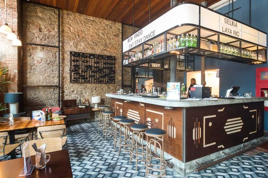 O espaço do bar do hotel com bebidas, luzes, cadeiras, mesas Onde se hospedar no Rock in Rio