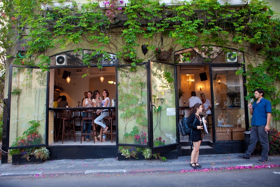 pessoas na calçada passando em frente a um restaurante com plantas na fachada Tel Aviv walking tour