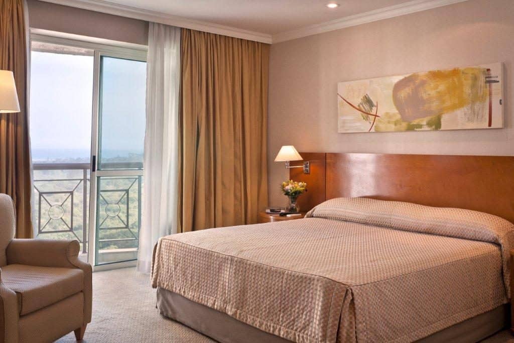 Quarto com luzes, cama, cadeira, quadro, cortina e sacada Onde se hospedar no Rock in Rio