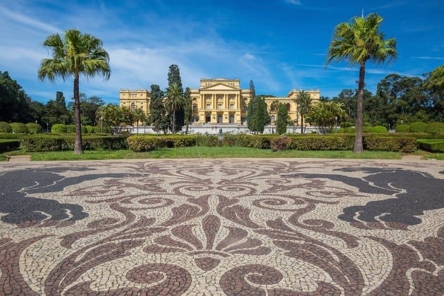 Ao fundo o museu de cor amarela rodeado de verde e coqueiros o que fazer em São Paulo