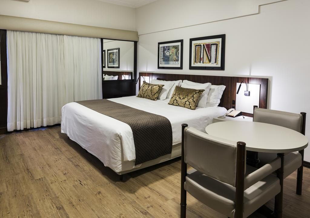 Acomodação com uma cama, mesa e cadeira, cortinas e quadros na parede Oktoberfest onde se hospedar