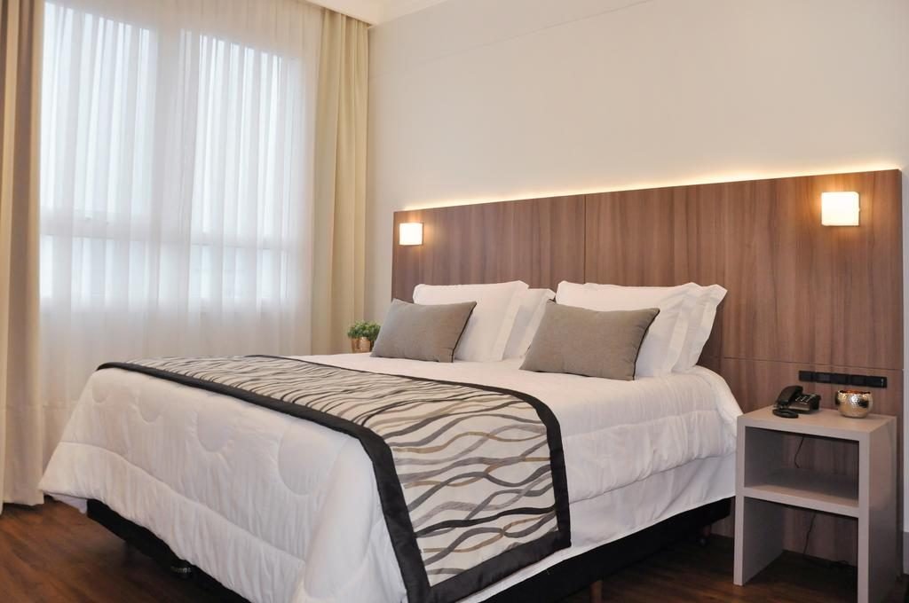 Um quarto com cama, cortina, criado mudo, telefone e iluminárias Oktoberfest onde se hospedar