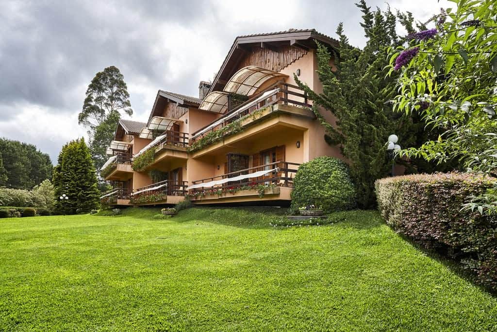 fachada das acomodações do hotel com árvores, arbustos, apartamento com sacada e chão com gramado O que fazer em Monte Verde MG