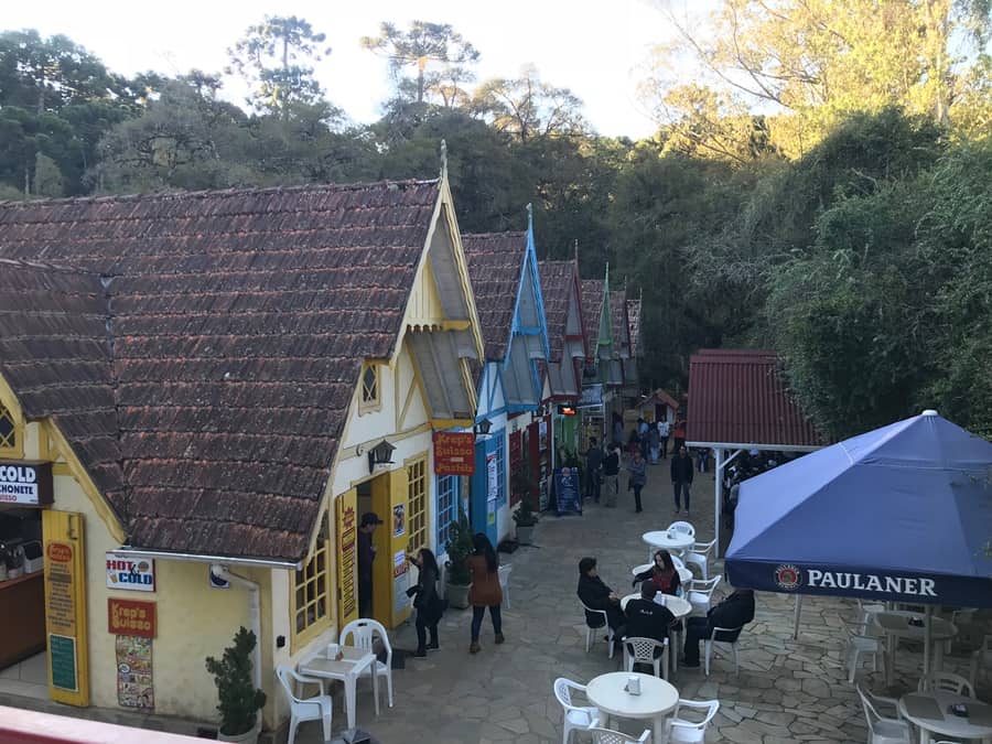Casinhas coloridas uma ao lado da outra com cadeiras e mesas a frente e pessoas caminhando O que fazer em Monte Verde MG