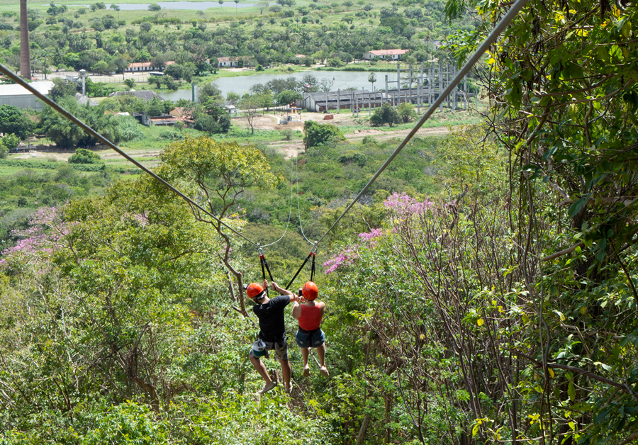 Casal se aventura descendo a tirolesa com árvores ao redor iPark tirolesa