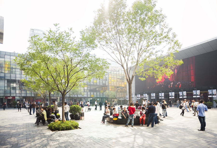 Praça com duas árvores, pessoas circulando e prédios de espelhos coloridos destinos para se inspirar
