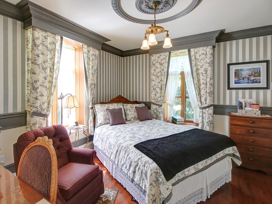 um quarto com cama, lustre, cortina, poltrona, criado mudo e paredes listradas passeios a pé