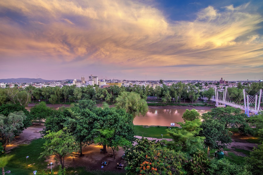 vista do alto de uma praça com muitas árvores e um lago, com o céu com nuvens passeios a pé