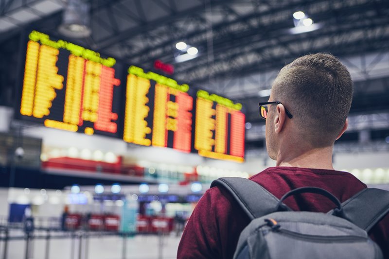 Homem olhando o painel de voos no aeroporto com uma mochila nas costas Passagens para Curaçao