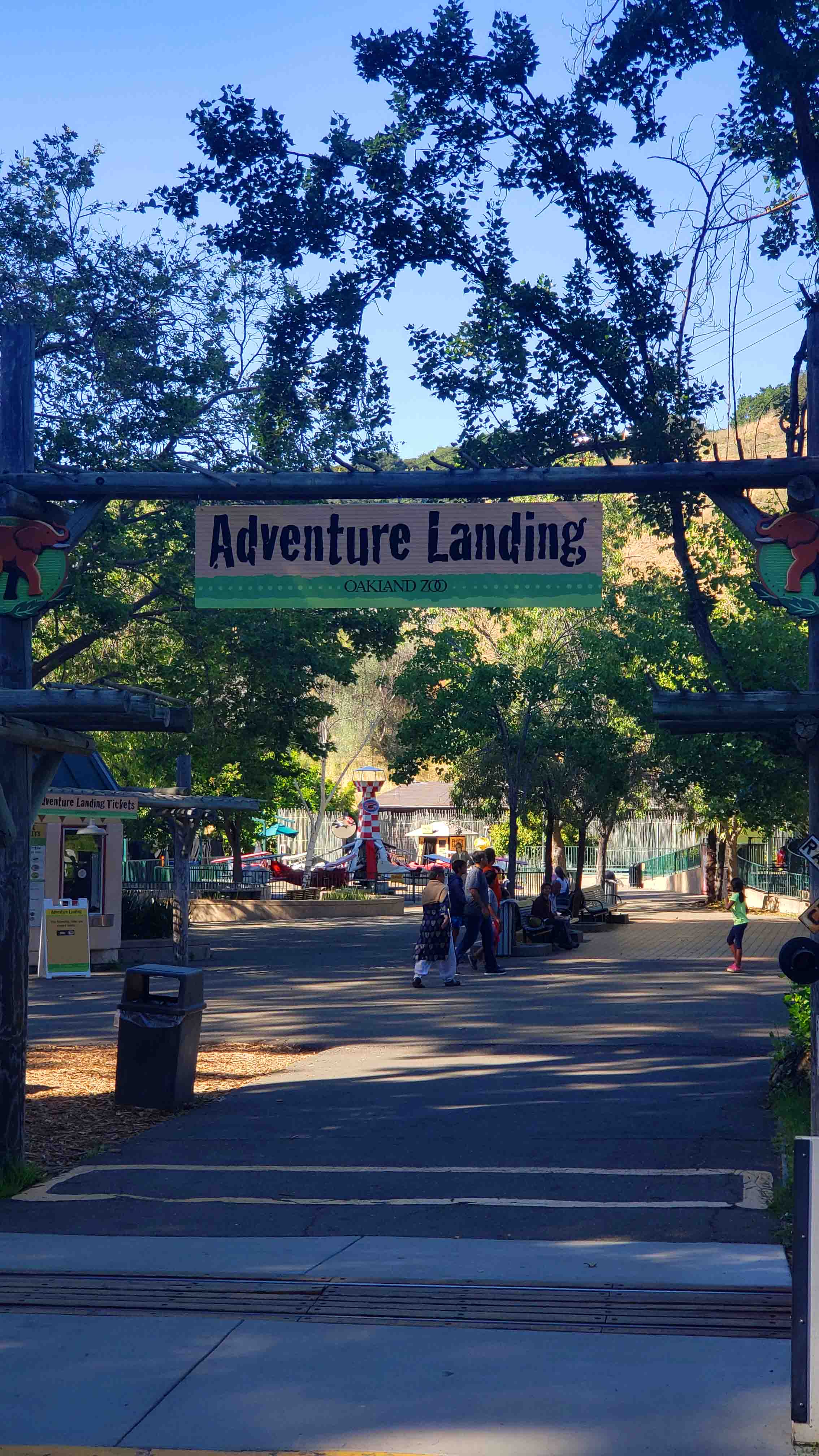 Entrada de um parque recreativo com pessoas e muitas arvores Oakland Zoo