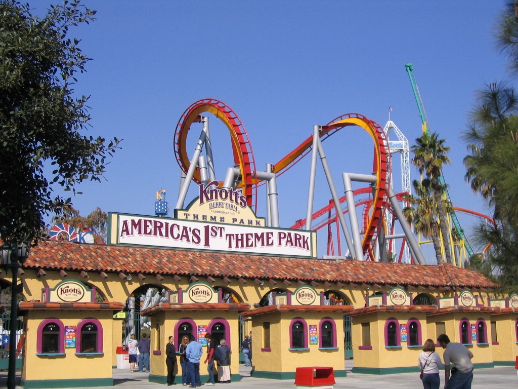 Pessoas em frente a predio amarelo com montanha russa ao fundo Anaheim