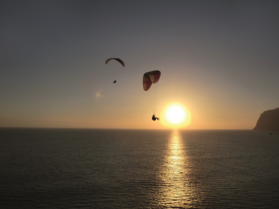 Duas pessoas fazendo voo durante o fim de tarde na praia Seguro viagem para esportes