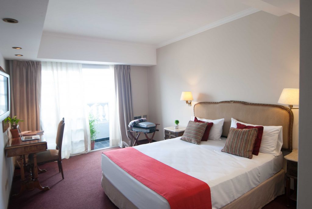 quarto com cama de casal, decoração em vermelho, mesa, cadeira, criado mudo e abajur Ramada by Wyndham Buenos Aires