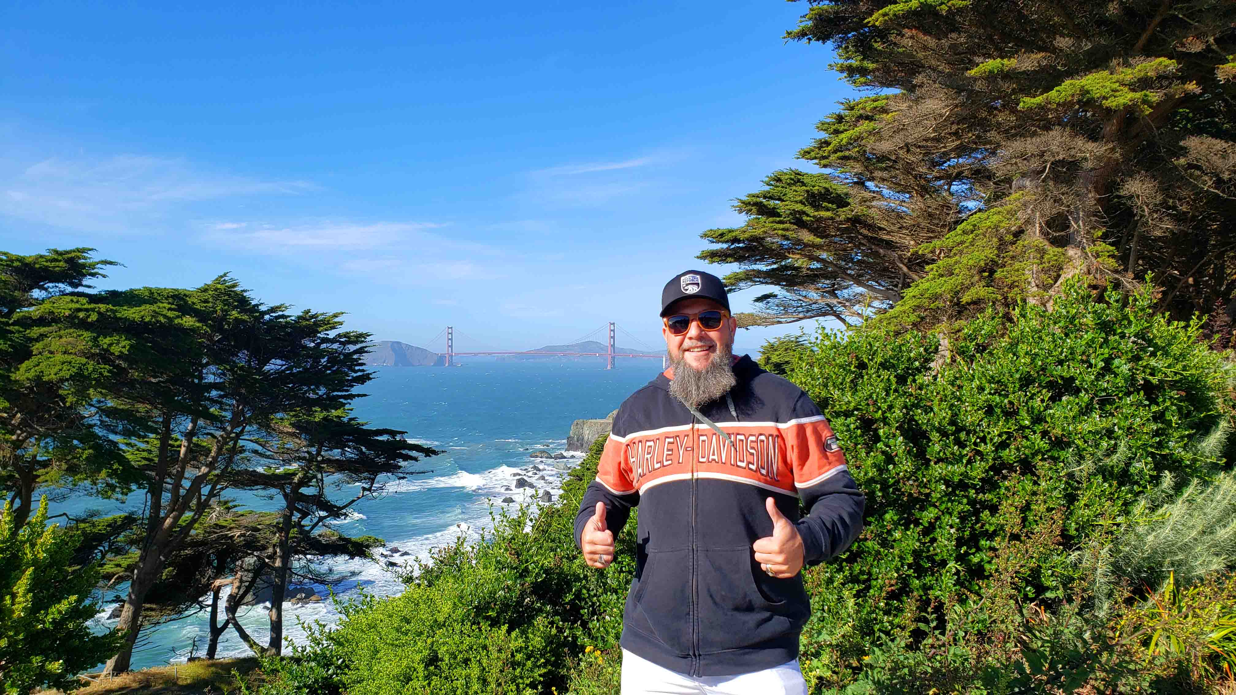 Homem posando para foto em meio a natureza com o mar e uma ponte Pose para foto