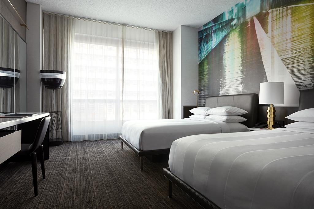 Um dos quartos do hotel com duas camas, quadro, abajur e mesa com cadeira