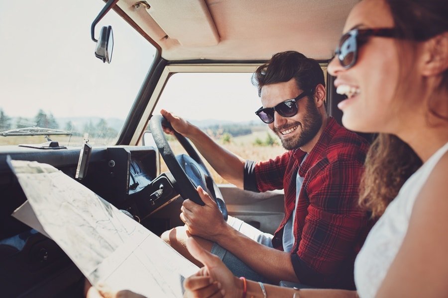 Homem e mulher dentro do carro com um mapa na mão Como alugar um carro na Rentcars