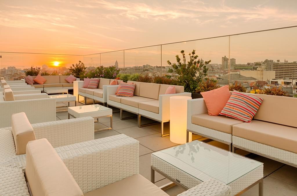 Vista do solário do Hotel Premium Porto Downtown com mesas, cadeiras, almofadas e por do sol Onde ficar em Porto