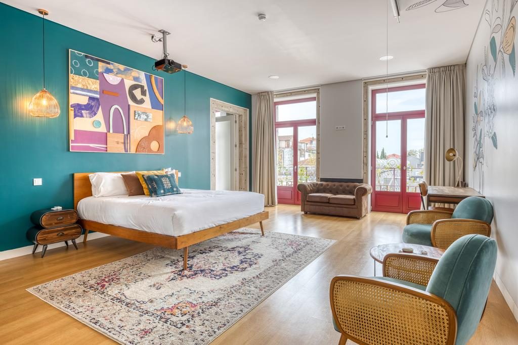 Um dos quartos do Selina Porto com cama, cadeiras, mesas, tapete, janela e cortina onde ficar em Porto