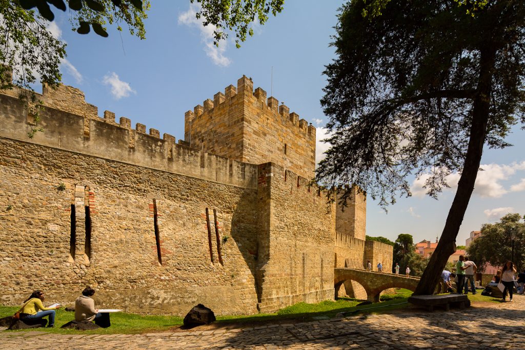 Castelo de São Jorge visto de fora, com árvore ao lado e duas pessoas sentadas O que fazer em Lisboa