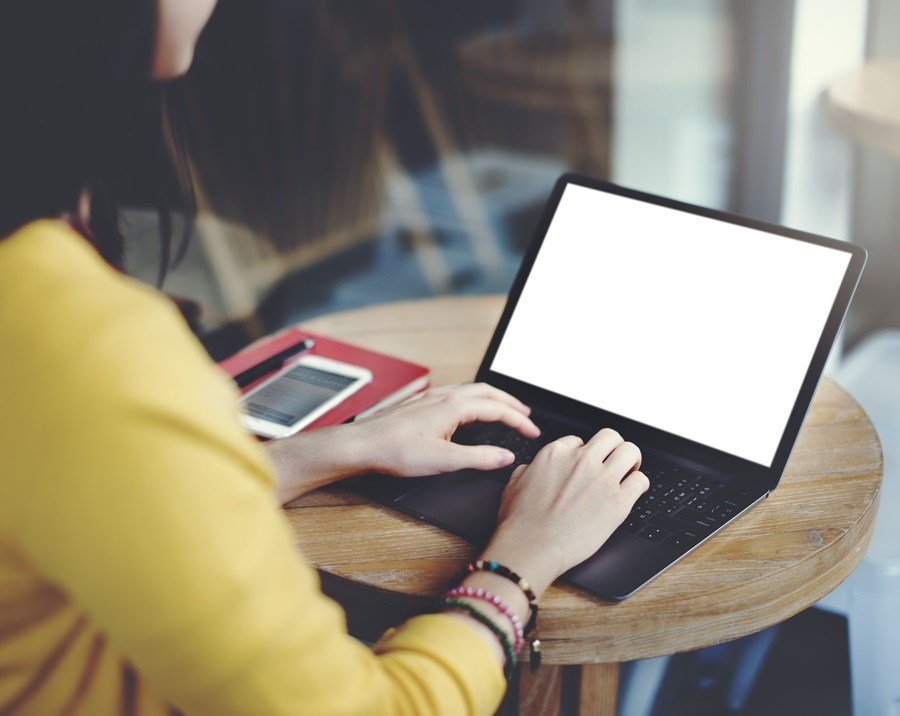 Mulher de amarelo usando o notebook em cima de uma mesa